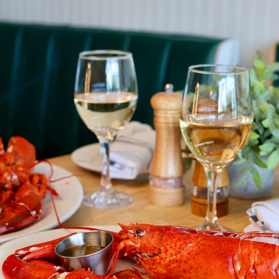 Two whole cooked lobsters with drawn butter and white wine on a restaurant table.