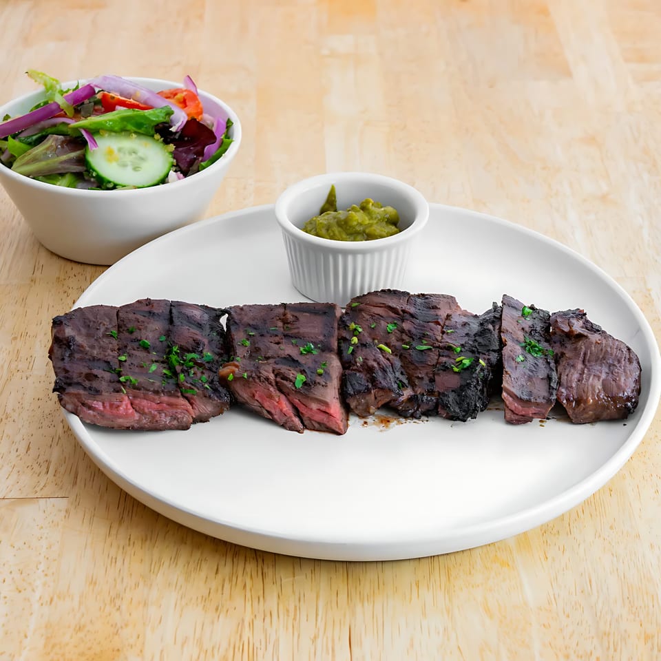 Grilled steak slices with a side salad and guacamole on a white plate.