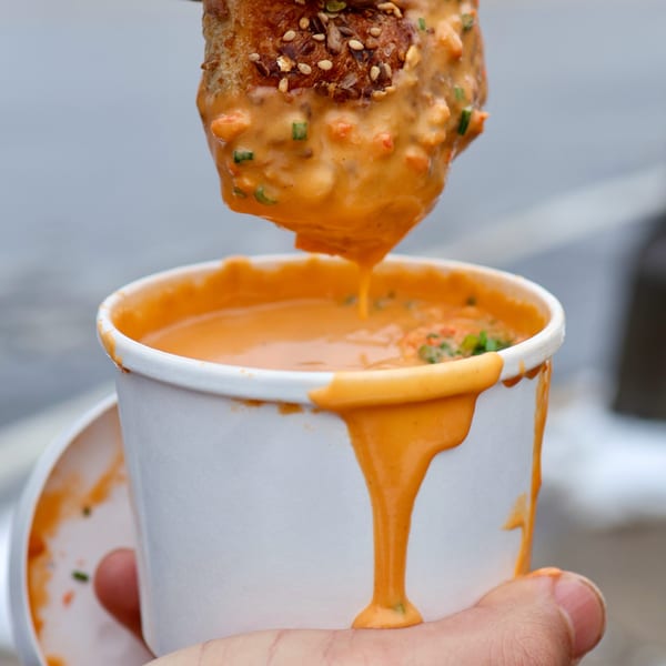 A hand dips a piece of bread into a cup of creamy orange soup, dripping down the side.