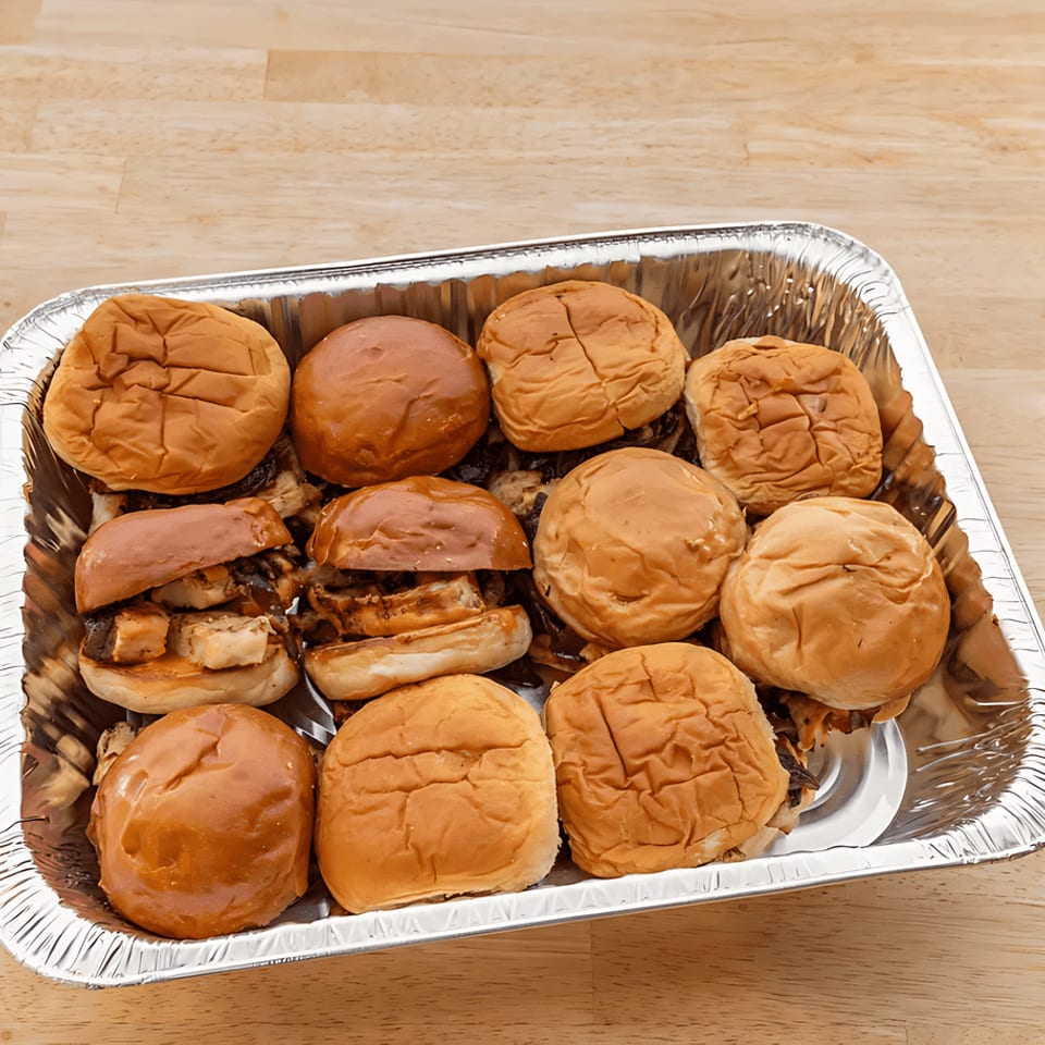 A foil tray filled with a dozen mini sliders, some open to show meat and onions.