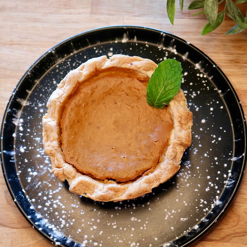 A mini pumpkin pie with a mint leaf on a black plate dusted with powdered sugar.