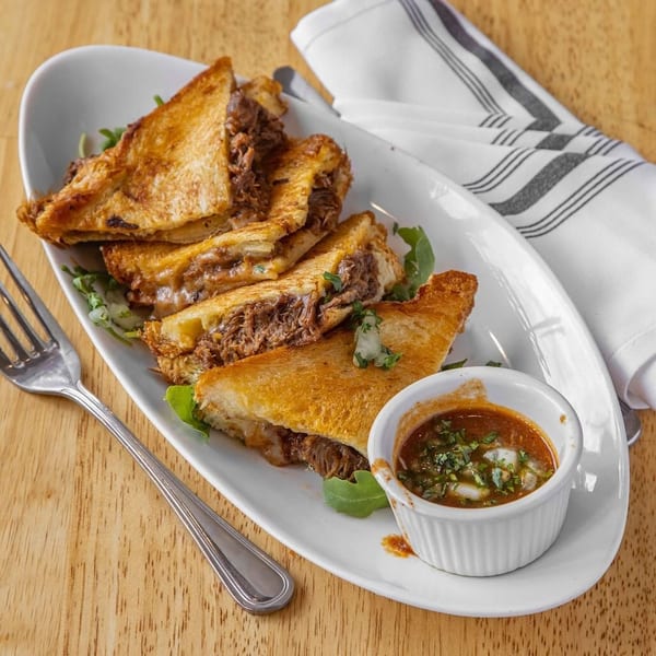 Golden grilled cheese sandwiches filled with shredded meat, served with a dipping sauce and fork.