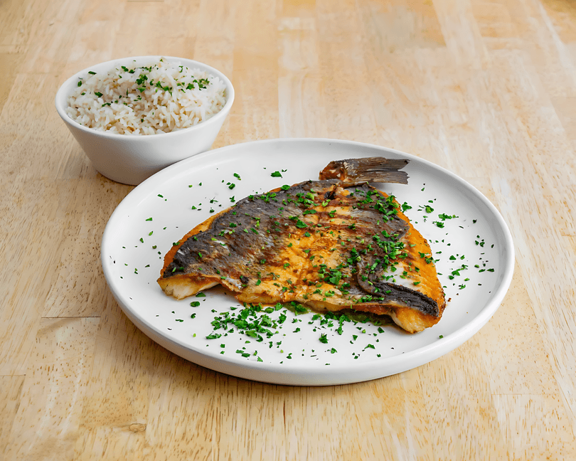 Grilled fish fillet with crispy skin and parsley, served with a side of white rice.