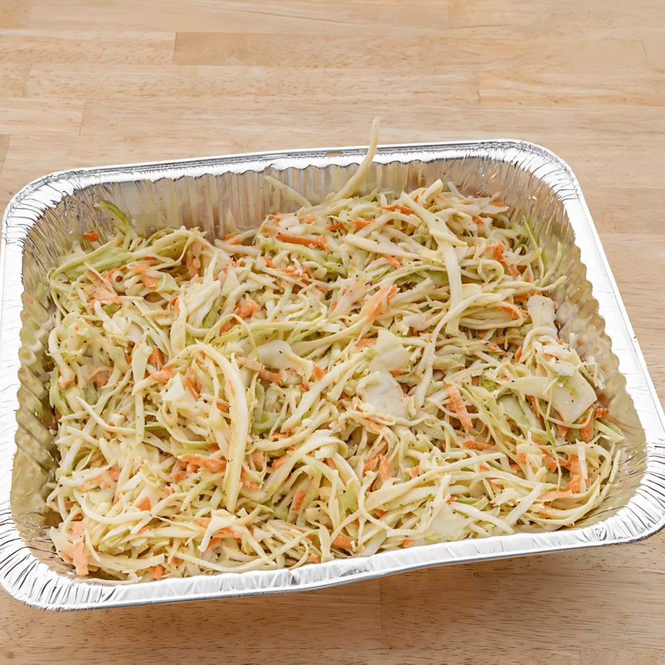 Creamy coleslaw with shredded cabbage and carrots in a large aluminum catering pan on a wooden table.