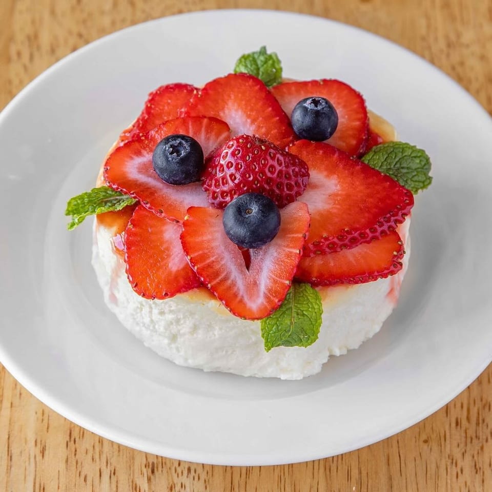 A white dessert topped with sliced strawberries, whole blueberries, and mint leaves on a white plate.
