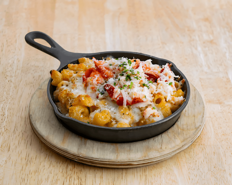 Lobster mac and cheese in a black cast iron skillet on a wooden serving board.